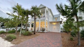 A two-story house with a covered front porch, a garage, and a landscaped front yard with palm trees. - The Sea And Me by Avantstay Heated Pool (Santa Rosa Beach)
