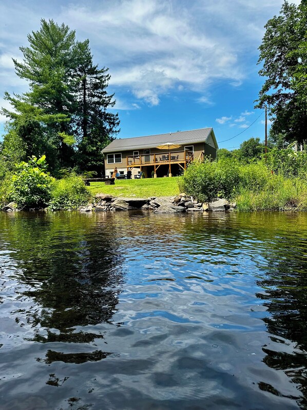 A house with a deck, a pond in front, and surrounding greenery.