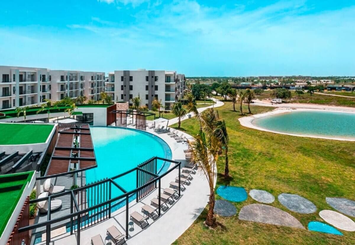 A resort with a large pool, multiple buildings, and a beach view.