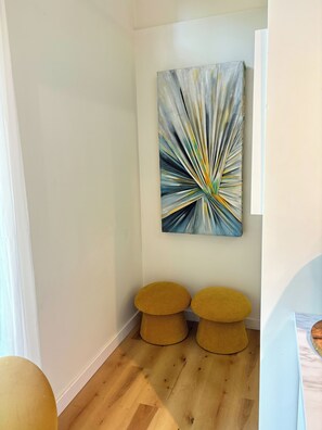 A hallway with a modern abstract painting, two round yellow stools, and wooden flooring. - 6 mins to DT St. Louis & Arch view. Complimentary wine,breakfast and golf mat. (Caseyville)
