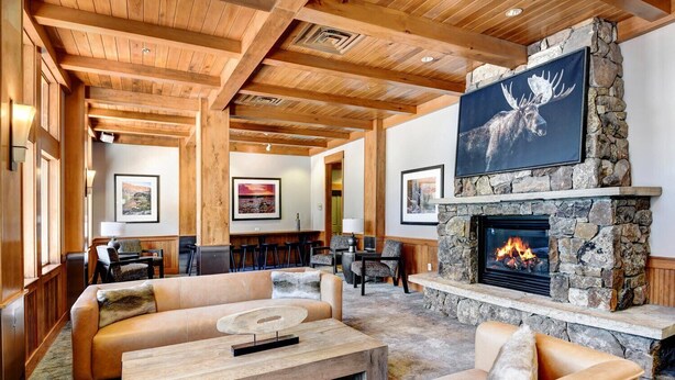 A cozy lounge area with a stone fireplace, wooden ceiling beams, and comfortable seating.