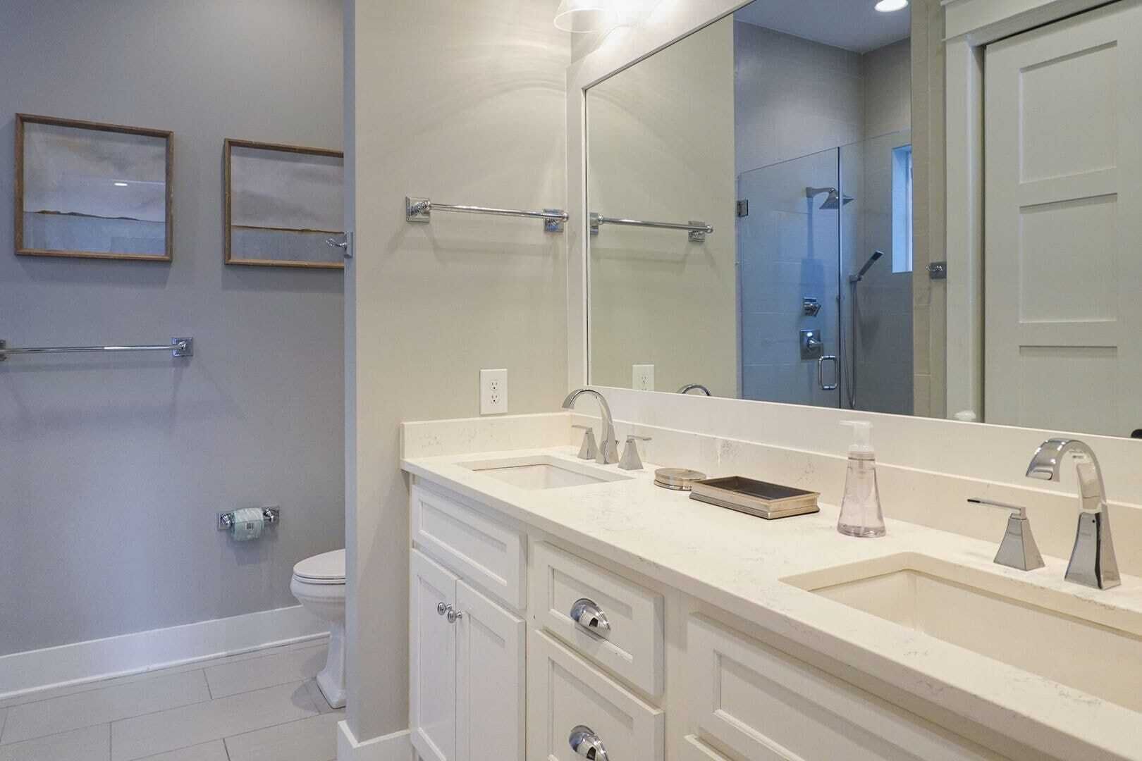 A modern bathroom with a double sink, a large mirror, and a toilet.