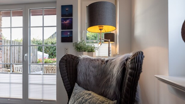 Een gezellige woonkamer met een rieten stoel, een lamp en uitzicht op een tuin door een schuifdeur.