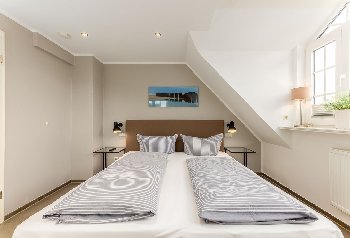Una habitación de hotel moderna con una cama grande, dos mesitas de noche, un buró, un ventanal con vistas y un cuadro en la pared.