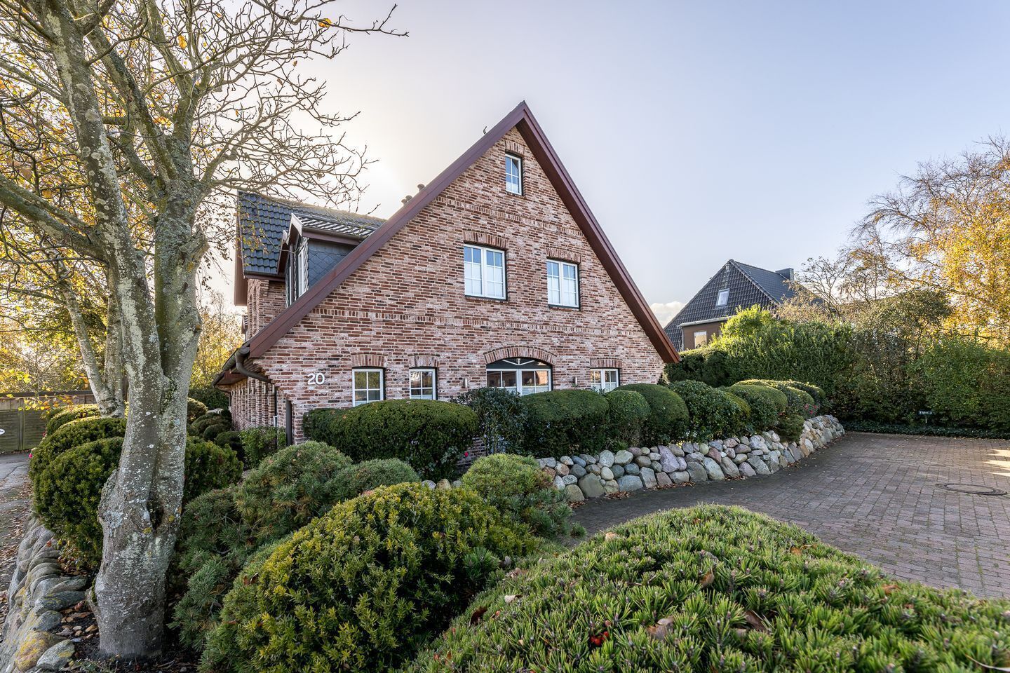 A brick house with a triangular roof, surrounded by well-maintained hedges and a stone wall.