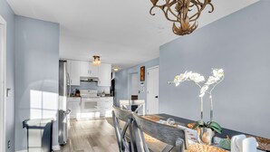 Una cocina moderna con armarios blancos, un refrigerador de acero inoxidable y un comedor con mesa y sillas de madera.