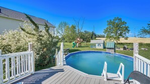 Una piscina con cubierta de madera y barandillas blancas, rodeada de árboles y césped.