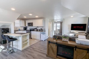 Una cocina moderna con armarios blancos, microondas y un comedor con taburetes de bar.