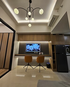 A modern kitchen with a flat-screen TV, two chairs, a dining table, and a black refrigerator. - Luxury condo with gym,WiFi,NETFLIX at Park Mckinley West, Venice, SM Aura BGC (Taguig)