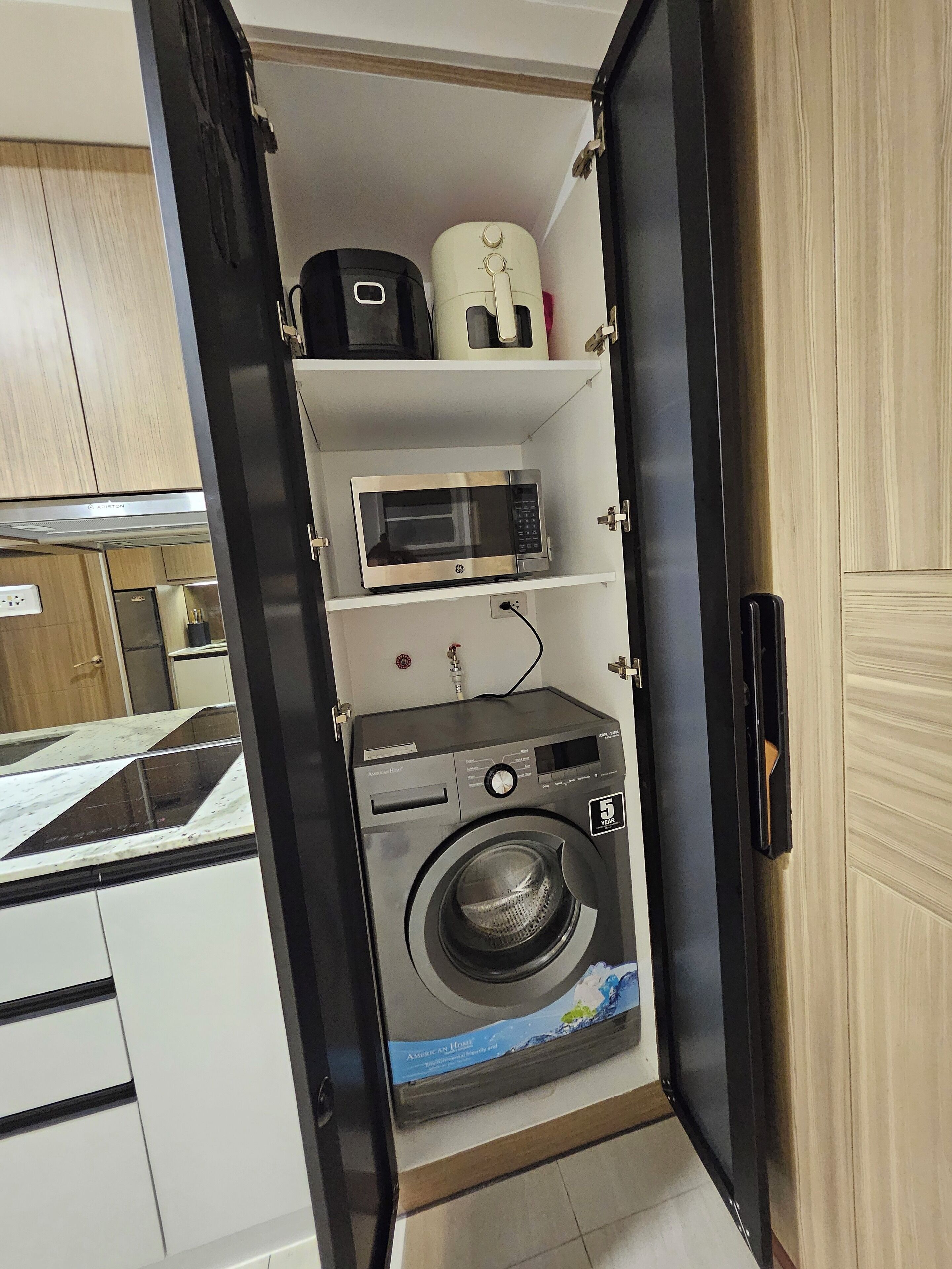 A compact kitchen with a built-in washing machine, a microwave, and a coffee maker on a shelf.