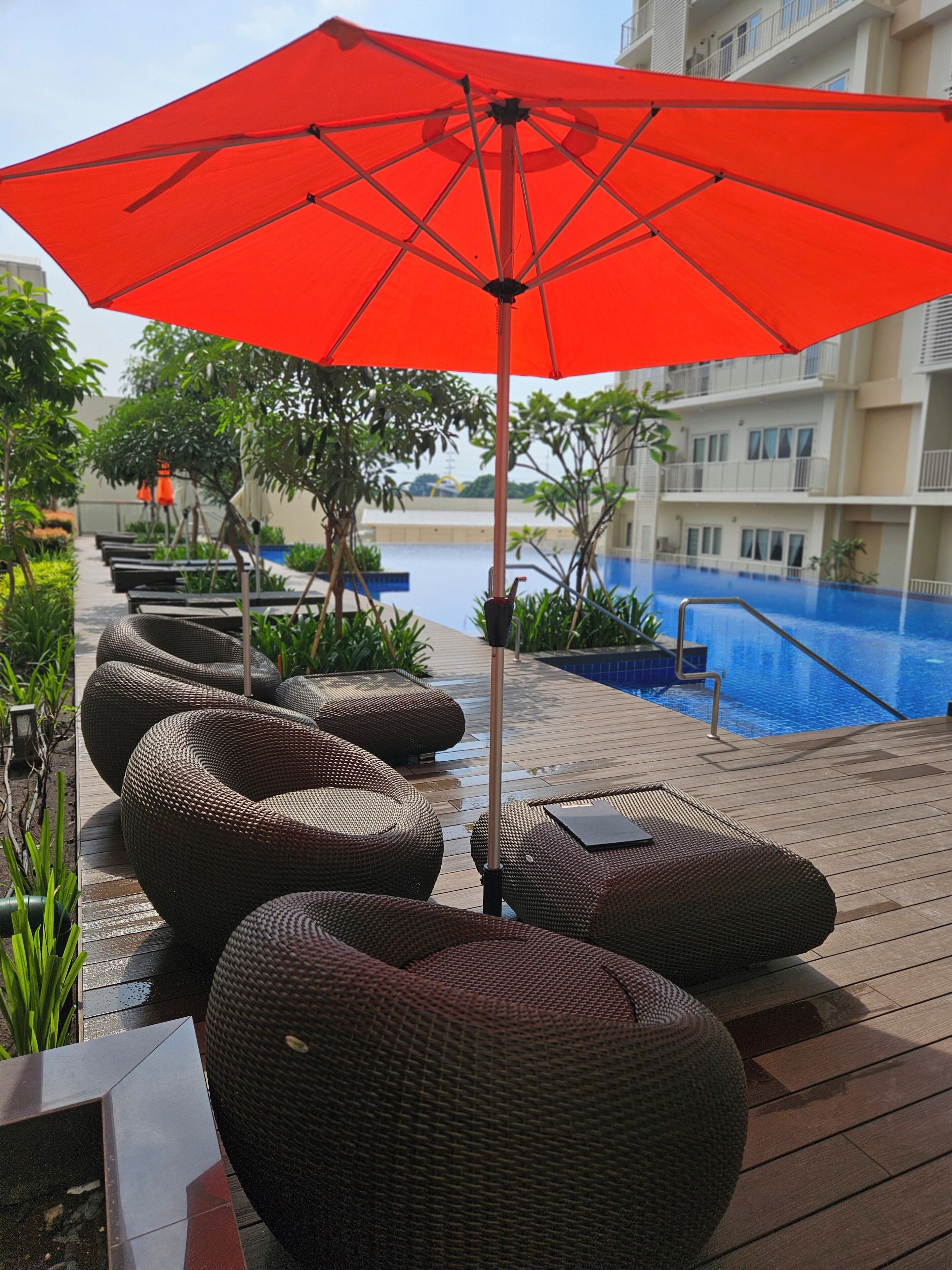 A poolside area with wicker lounge chairs and a red umbrella.