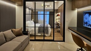 A modern hotel room with a large bed, a desk, a TV, and a sliding door leading to a bathroom. - Luxury condo with gym,WiFi,NETFLIX at Park Mckinley West, Venice, SM Aura BGC (Taguig)