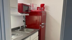 Una cucina compatta con mobili bianchi, un frigorifero rosso, un forno a microonde e una macchina da caffè.