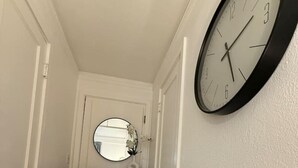Un corridoio con pavimento in legno, una porta bianca, un comò con cassetti e un orologio a parete rotondo.