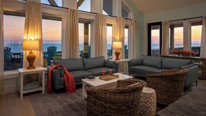 A modern living room with two sofas, a coffee table, and wicker furniture. Large windows offer a view of the sea. - Luxurious Beachfront 4BR with Pool, Hot tub, Elevator (Port Bolivar)