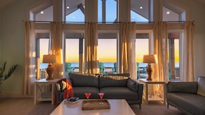 A spacious living room with a large sofa, two side tables with lamps, a coffee table with drinks, and large windows offering a view of the sea. - Luxurious Beachfront 4BR with Pool, Hot tub, Elevator (Port Bolivar)