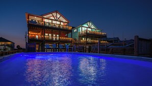 A two-story building with a pool, featuring a balcony with chairs and a sign. - Luxurious Beachfront 4BR with Pool, Hot tub, Elevator (Port Bolivar)