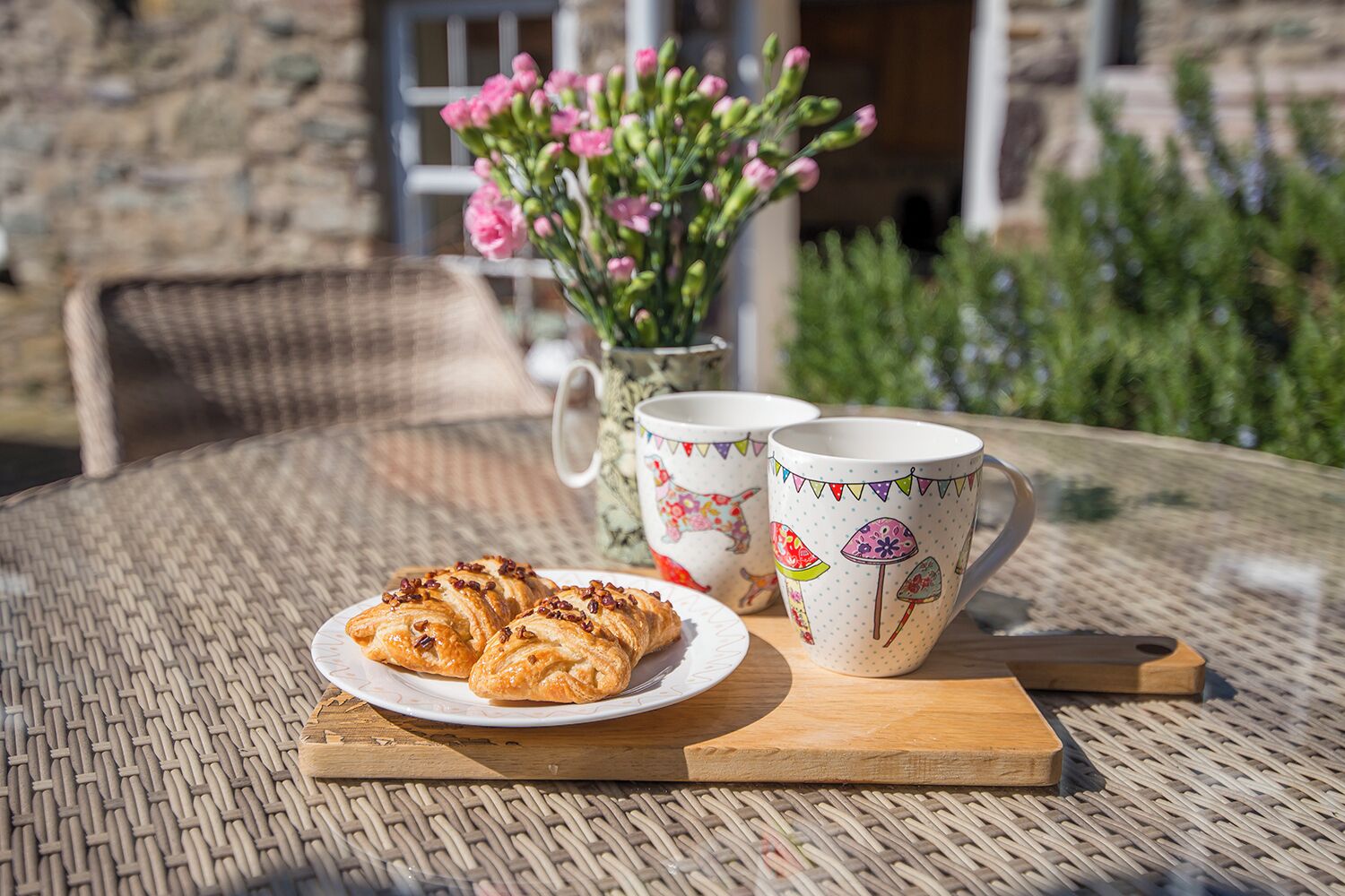 Een rieten tafel met een bord croissants en twee mokken met bloemenmotieven.