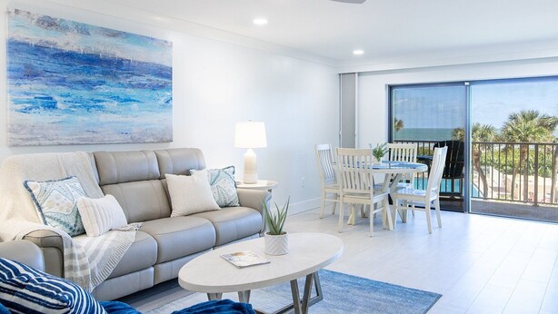 Un salon moderne avec un canapé, une table basse et un coin repas avec des chaises. Un tableau orne le mur et une grande fenêtre offre une vue sur l’extérieur.