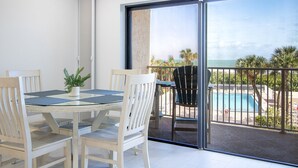 Un balcon doté d’une porte-fenêtre donnant sur une piscine, une table à manger avec des chaises et une vue sur l’océan.