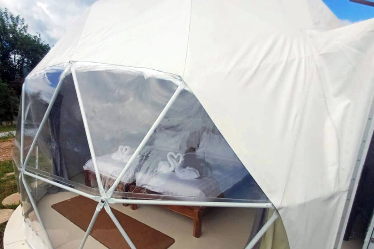 A dome-shaped tent with a transparent ceiling, a bed, and a small table.