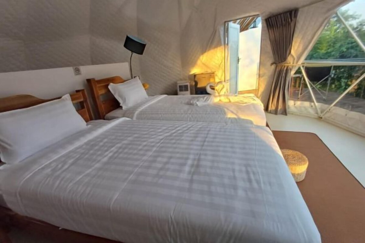 A tent-style room with two beds, a flat-screen TV, and a window with curtains.