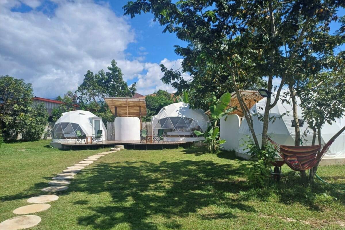 A series of dome-shaped structures with a central open area, surrounded by a grassy lawn and a wooden deck.