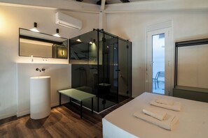 Un baño moderno con un lavamanos grande, cabina de ducha de vidrio, banco y cama con toallas.