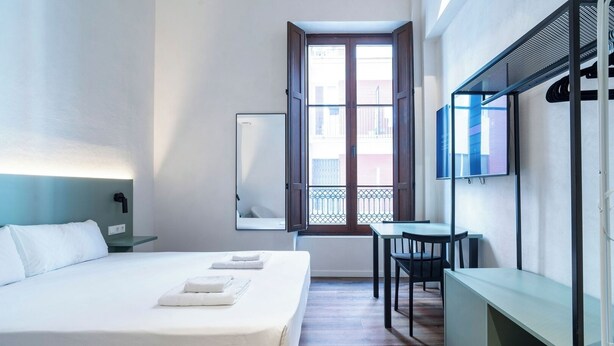 A hotel room with a bed, a desk, a chair, a TV, and a balcony with a view.