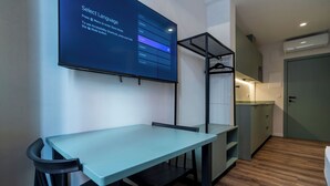 A modern, minimalist room with a light blue table and black chairs, a black hanging rack, and a small kitchenette.