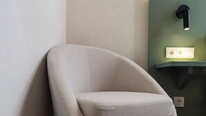 Un sillón de esquina con un cojín, ubicado frente a una pared con interruptor de luz y toma de corriente.