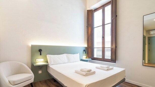 Habitación de hotel ordenada con cama, lámparas de noche, una silla y ventana con vistas.