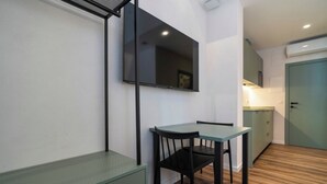 Una pequeña cocina americana con una mesa y una silla, un televisor montado en la pared y una puerta que da a otra habitación.