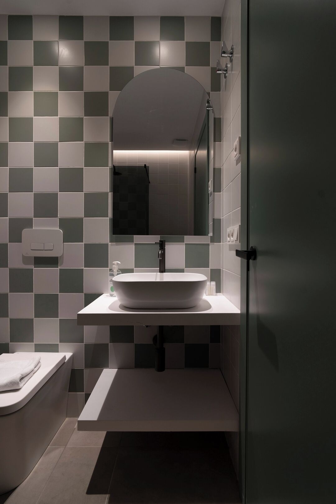 A modern bathroom with a white sink, a mirror, and a tiled wall.
