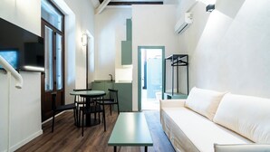 Un espacio habitable compacto con sofá, una mesa de comedor con sillas, una pequeña cocina y un vestidor.