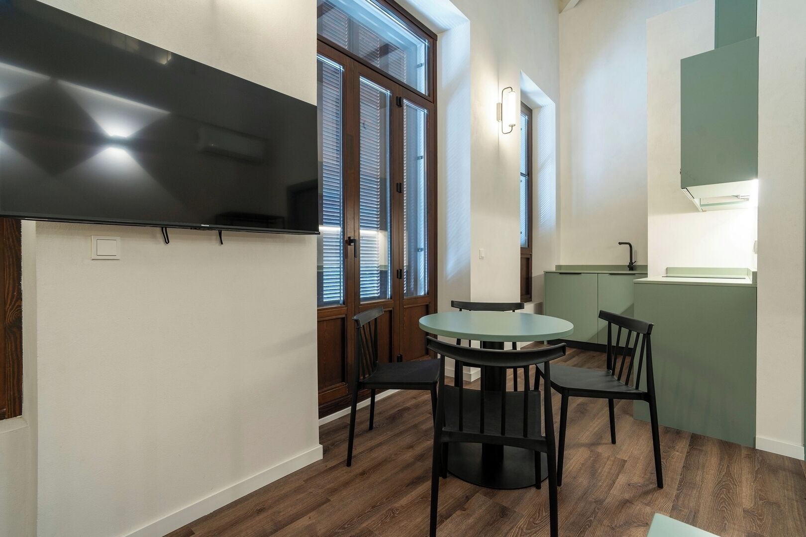 Una cocina moderna con encimera verde, horno integrado y ventana con persianas.