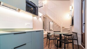 Una cocina moderna con microondas integrado, un comedor con mesa redonda y sillas, y una escalera que conduce a un nivel superior.