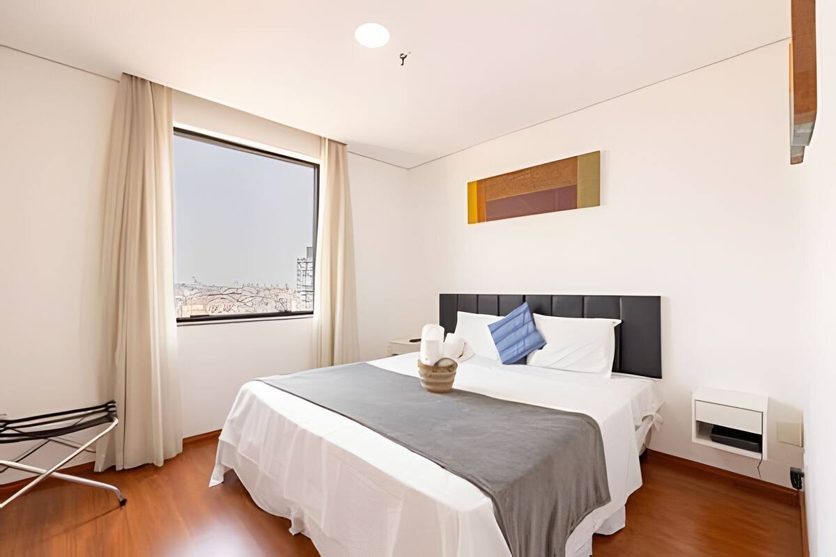 Ein Hotelzimmer mit großem Fenster, einem Bett mit weißer Bettwäsche, einer grauen Decke und einem modernen Kopfteil.