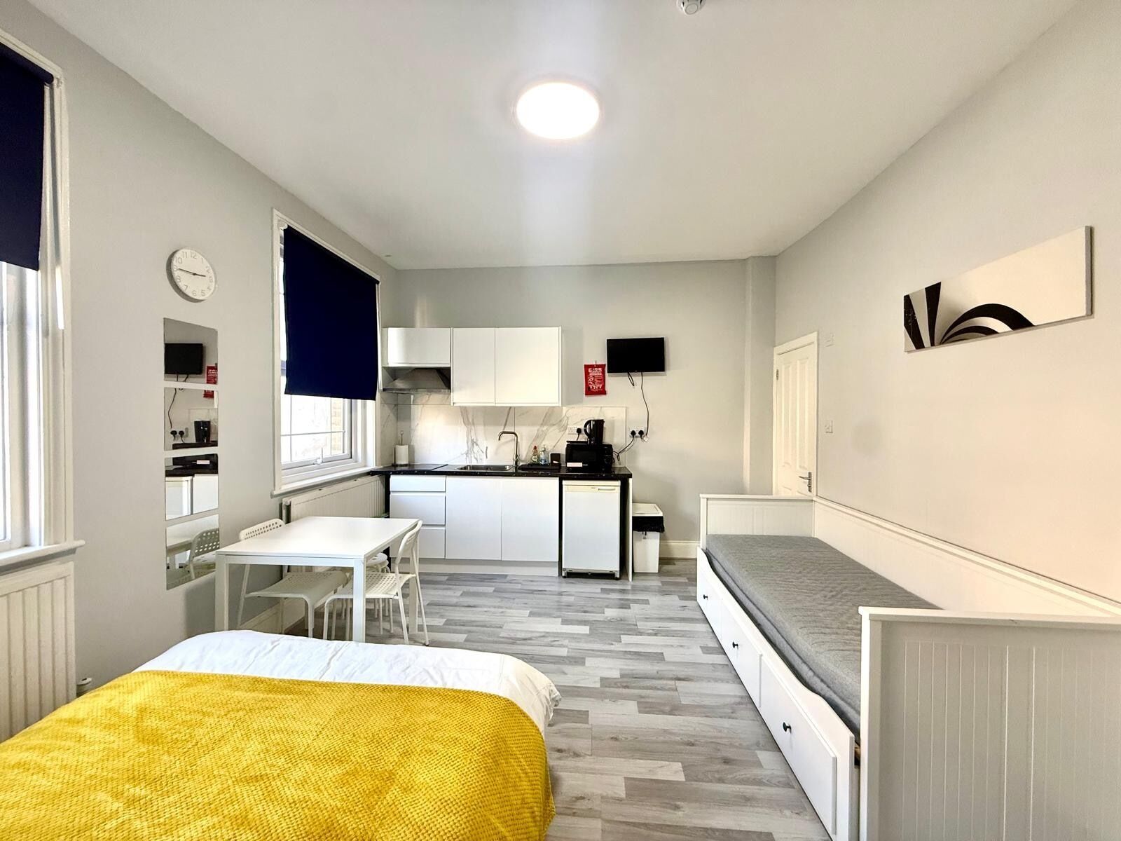 Una habitación pequeña con cama, una mesita, kitchenette y ventana.