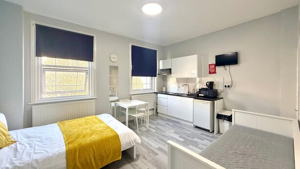A compact room with a bed, a small table, a kitchenette, and a TV.