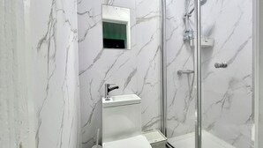 A modern bathroom with a marble wall, a glass shower enclosure, and a white sink.