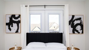 Une chambre à coucher avec un grand lit, deux tables de chevet et deux tableaux abstraits accrochés aux murs.