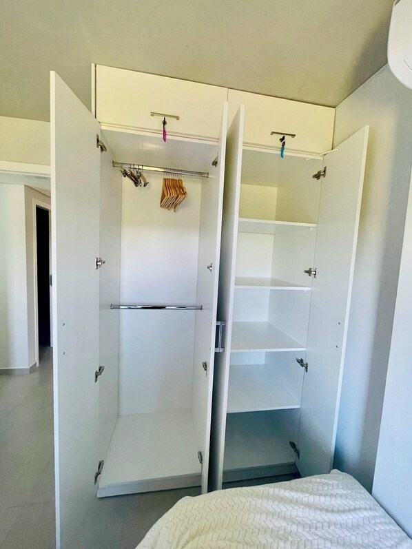 A room with a bed, a wardrobe with open doors, and a hanging coat rack.