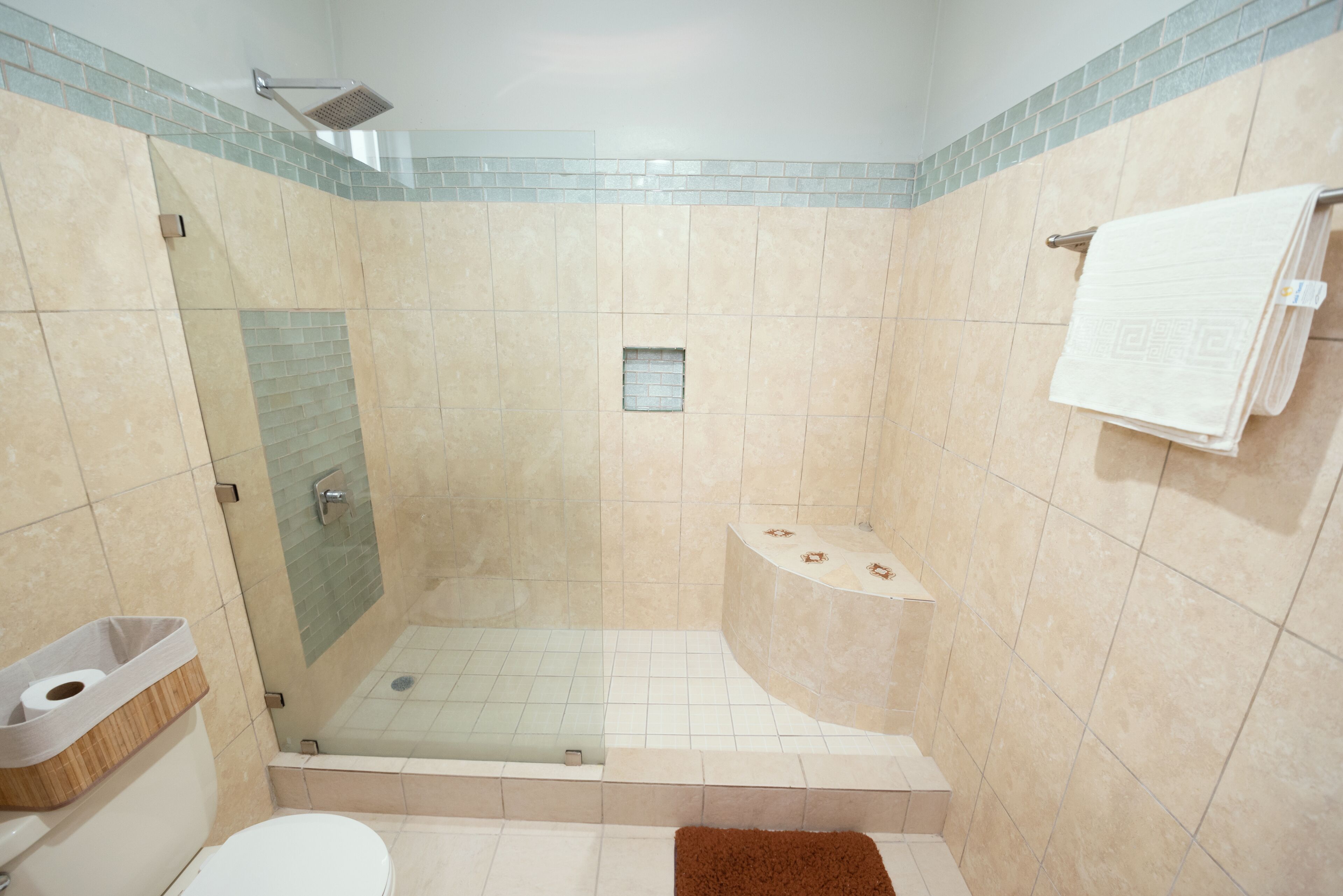 A bathroom with a glass-enclosed shower, a toilet, and a sink with a wooden tray.