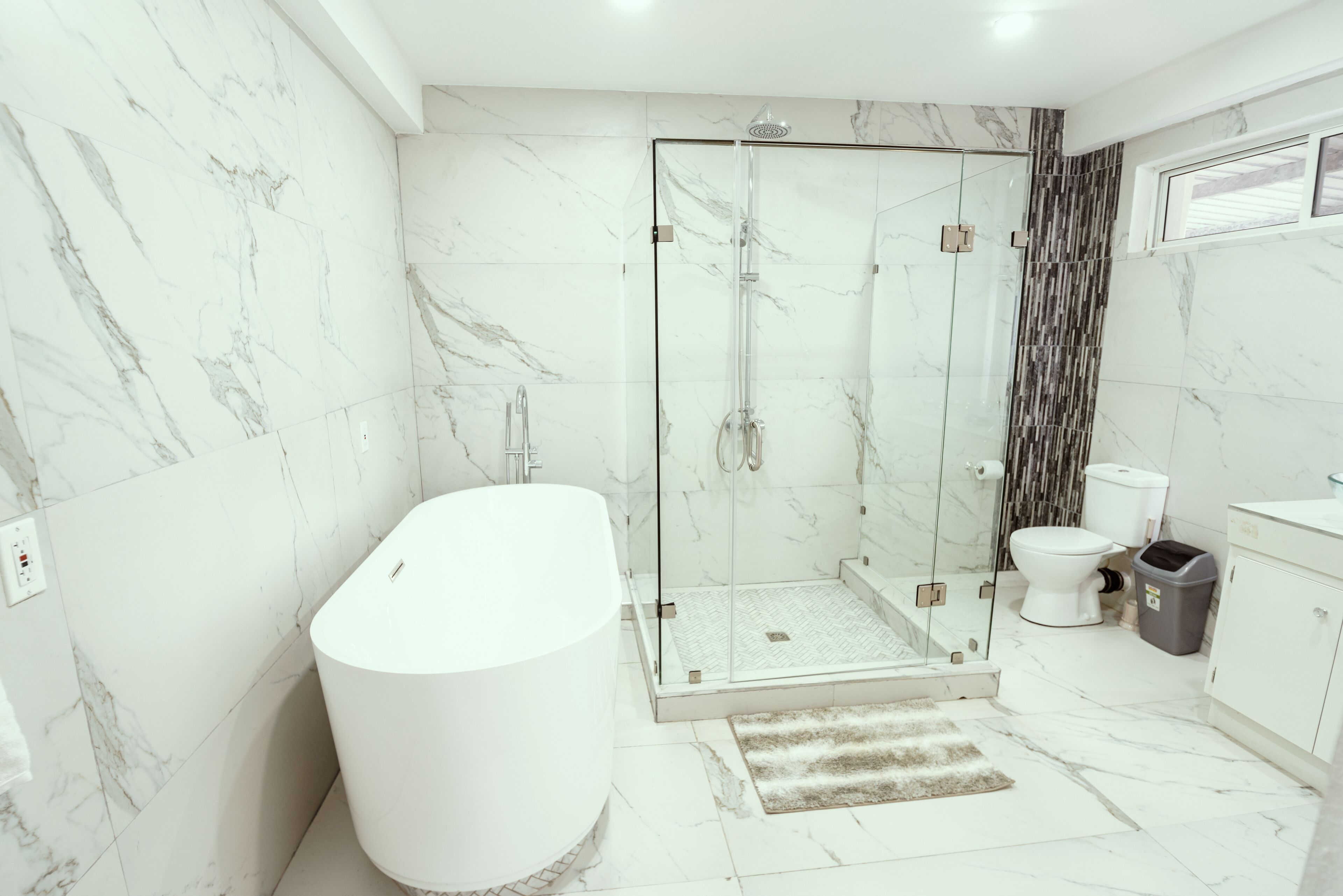 Un baño moderno con ducha envuelta en vidrio, una bañera independiente y un inodoro.