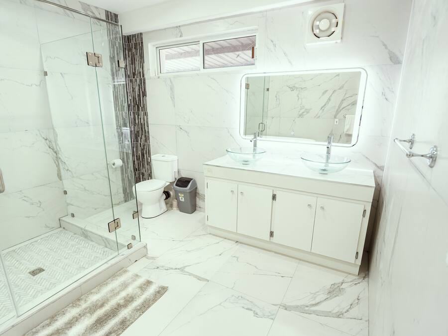 Ein modernes Badezimmer mit einer Duschkabine, einem großen Spiegel und einem Marmorboden.