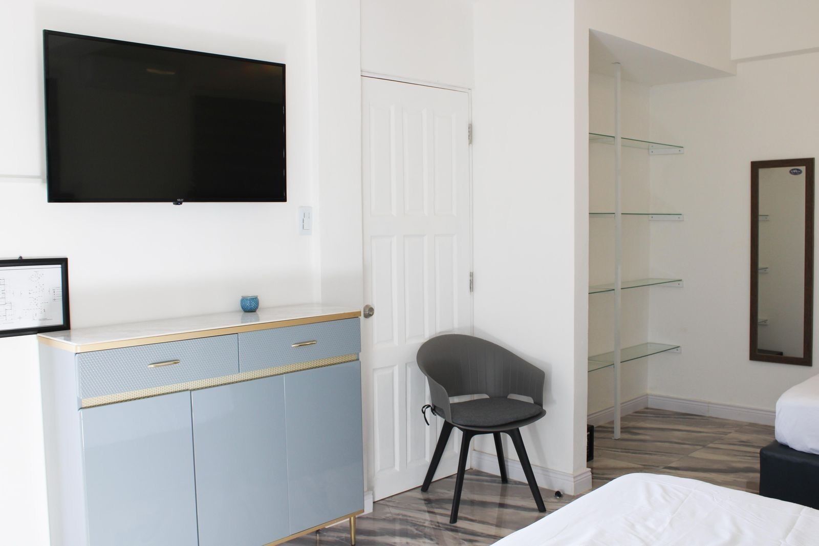 A bedroom with a bed, a desk with drawers, a chair, a television mounted on the wall, and a mirror on the wall.