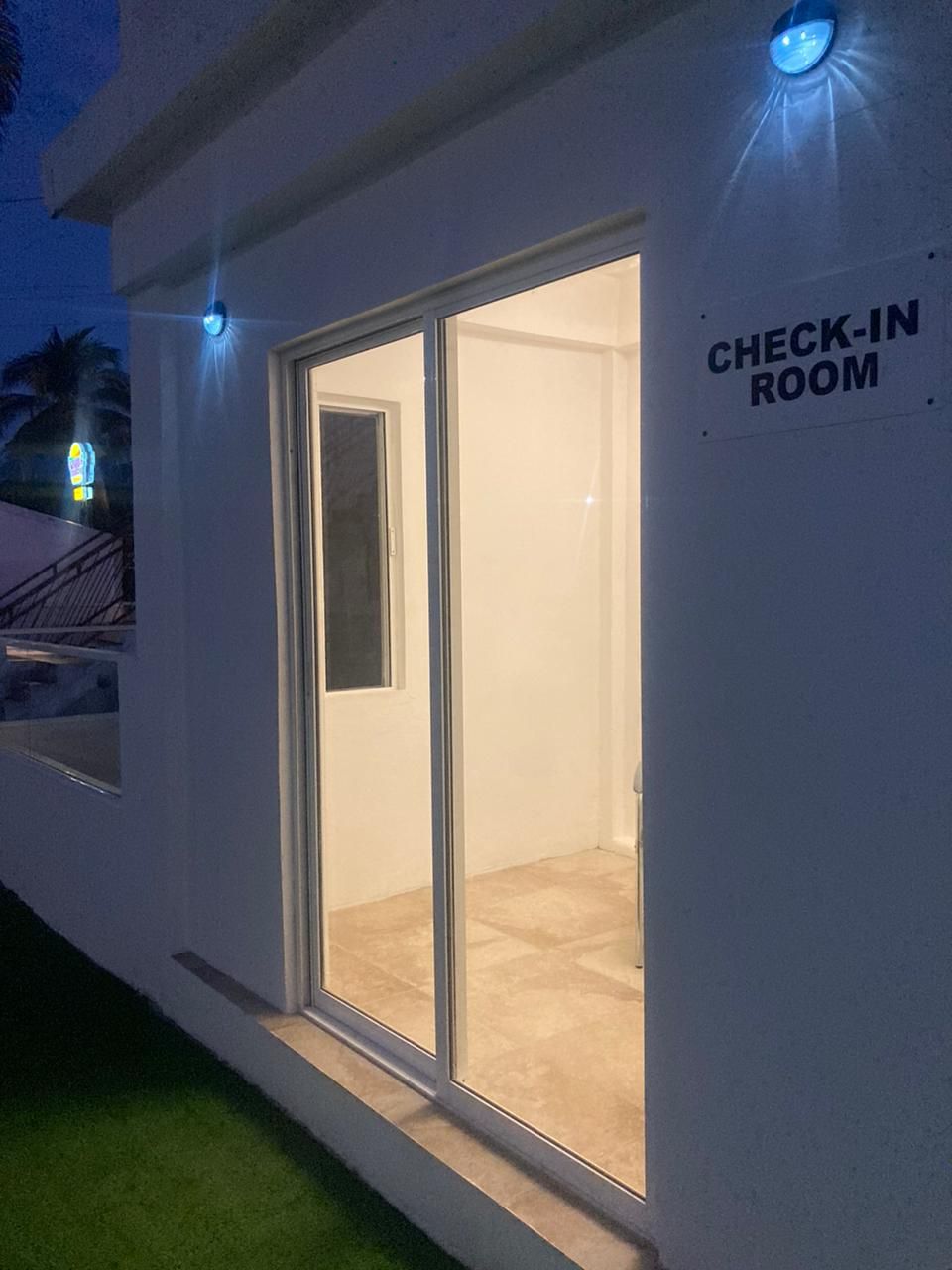 Entrada a una habitación de hotel con un cartel que dice 'CHECK-IN ROOM' y un puerta de vidrio que da al interior.