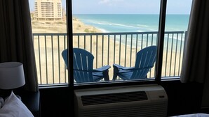 Ein Hotelzimmer mit einem Bett, einem Fenster mit Blick auf Strand und Meer sowie zwei blauen Stühlen davor.