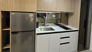 A modern kitchen with a stainless steel refrigerator, a sink with a faucet, and wooden cabinets. - Luxury condo with gym,WiFi,NETFLIX at Park Mckinley West, Venice, SM Aura BGC (Taguig)